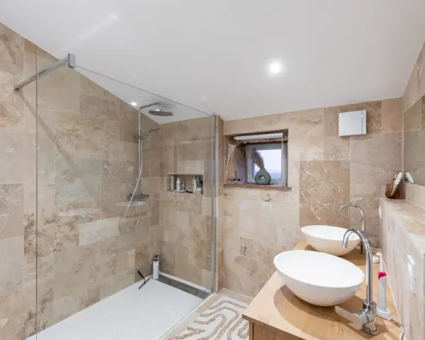Salle de bain moderne avec douche à l'italienne, double vasque et carrelage en pierre naturelle. Un projet réussi pour refaire la salle de bain.
