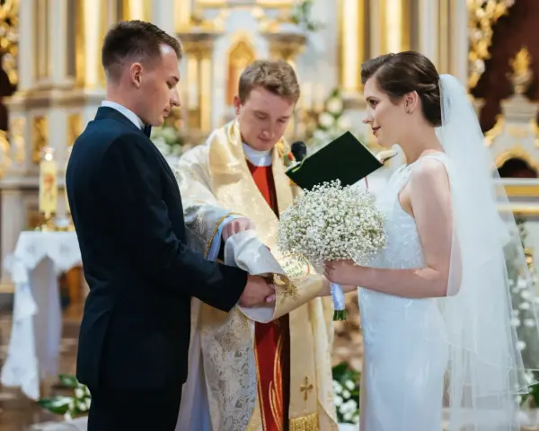 Panna młoda w welonie i z bukietem, pan młody w garniturze, podczas ceremonii ślubnej w kościele.