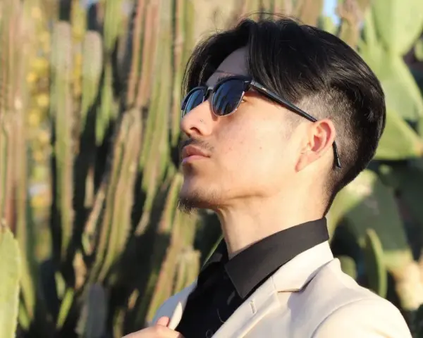 Uomo con abito beige e camicia nera, occhiali da sole, tra i cactus. Un look elegante per ogni occasione.