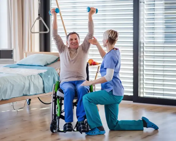 Starszy mężczyzna w wózku ćwiczy z hantlami pod okiem fizjoterapeutki. Czy rehabilitacje można odliczyć od podatku?