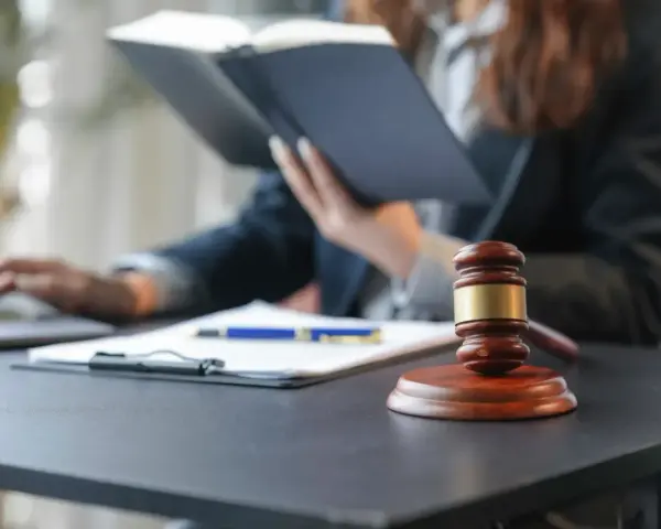 Sądowy młotek i dokumenty na biurku. Prawnik w tle studiuje akta, zastanawiając się, czy radca prawny może być obrońcą.