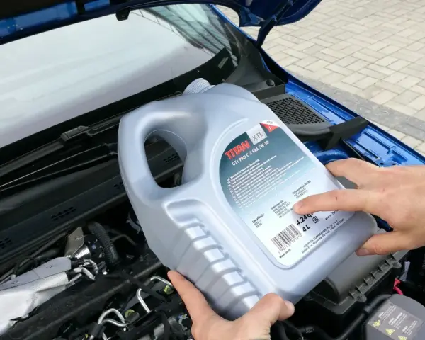 Osoba trzymająca kanister oleju silnikowego TITAN GT1 PRO C-3 SAE 5W-30 nad silnikiem. Czy można mieszać oleje silnikowe? Sprawdź specyfikacje!