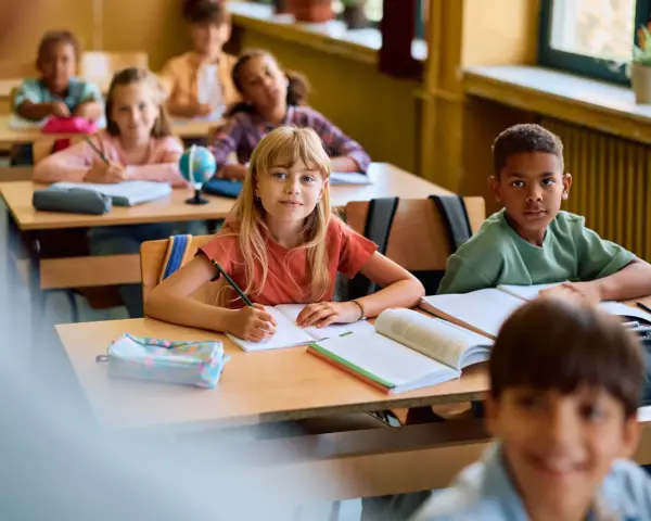 Dzieci w klasie skupione na lekcji. Uczennica pisze w zeszycie, obok niej leży piórnik. To pokazuje, co na koncentrację u dzieci: nauka i zaangażowanie.