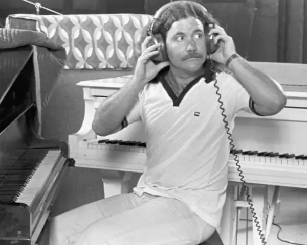 Billy Powell hört mit Kopfhörern Musik, während er neben einem Klavier sitzt.