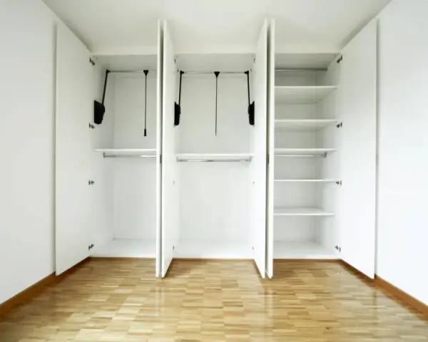 Interno di un armadio bianco a tre ante, vuoto, con ripiani e barre appendiabiti. Un esempio di come costruire un armadio funzionale.