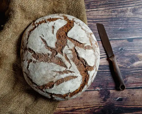 Pan casero rústico sobre arpillera, listo para cortar con un cuchillo. Una delicia para tu receta de pan casero.