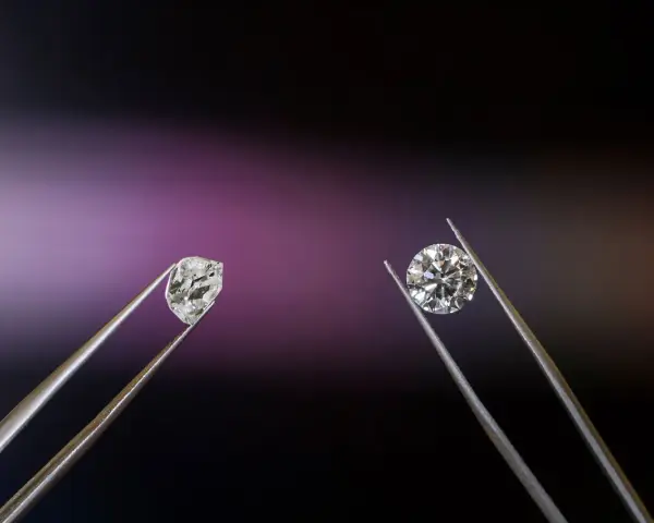Dwa kamienie szlachetne w pęsecie: surowy brylant i oszlifowany diament.