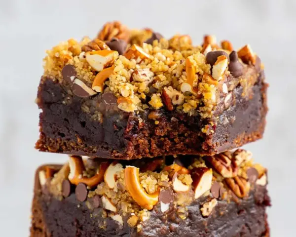 Zwei gestapelte, saftige fudge brownies, garniert mit Brezelstückchen, Nüssen und Schokostückchen.