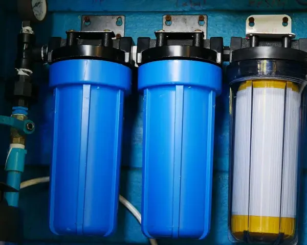 System filtrów do wody, który oczyszcza wodę. Dwa niebieskie filtry i jeden przezroczysty z białym wkładem.