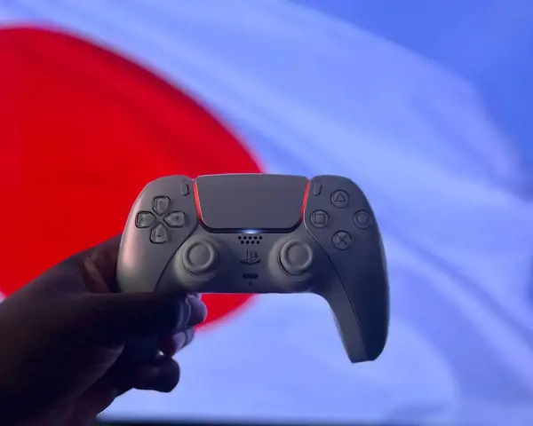 Dłoń trzyma biały kontroler DualSense. Czy gry z PS5 działają na PS4? To pytanie nurtuje graczy.