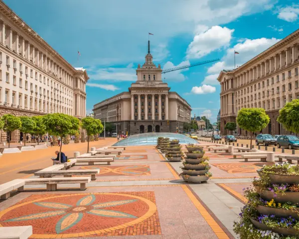 Słoneczna pogoda w Bułgarii w lipcu. Sofia, plac przed budynkiem Narodowego Zgromadzenia, z drzewami i kwiatami.