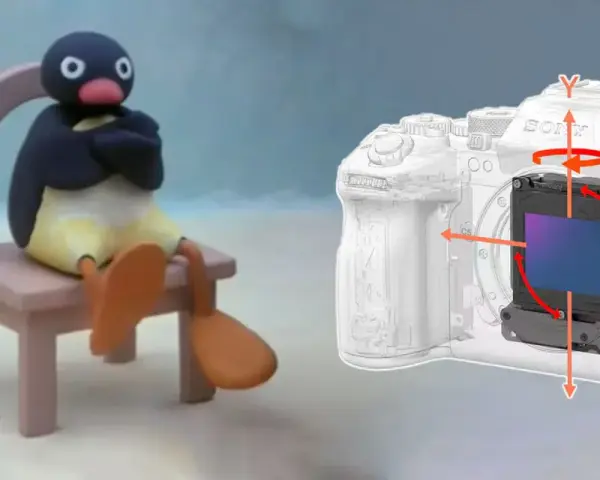 Pingu siedzi na krześle obok aparatu z widocznym mechanizmem optycznej stabilizacji obrazu, który kompensuje ruchy.