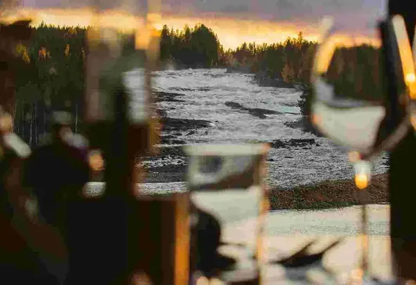 Storforsen camping: en brusande fors i solnedgången, med skog och träd som ramar in. Mysig belysning i förgrunden.