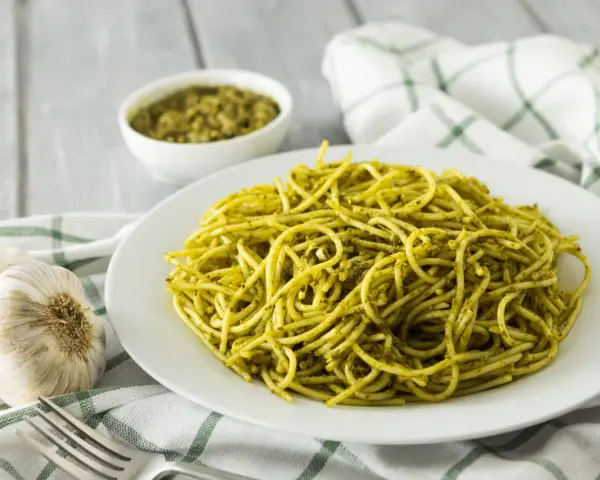 Pyszny makaron z pesto, podany na białym talerzu, obok czosnku i miseczki z sosem.