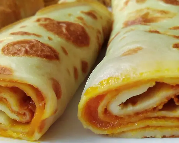 Dwa zwinięte naleśniki z dżemem, apetycznie wyglądające, z widocznym pomarańczowym nadzieniem.