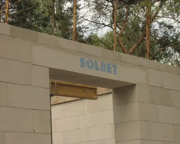 Ściana z bloczków betonowych z widocznym nadprożem marki SOLBET. Widać, jak nadproże ile powinno zachodzić, by zapewnić stabilność konstrukcji.