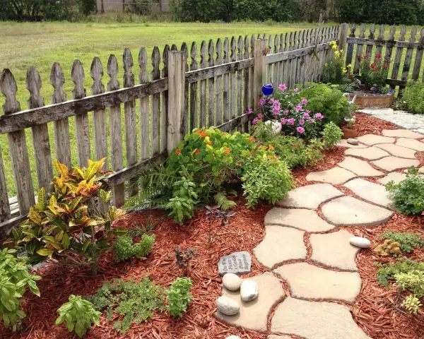 Natürliche Steinplatten formen einen geschwungenen Gartenweg, umgeben von bunten Blumen und grünen Pflanzen. Tolle Gartenweg Ideen für ein idyllisches Zuhause.