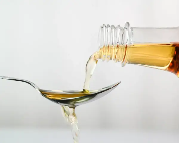 Apfelessig wird aus einer Flasche auf einen Löffel gegossen. Ein Tropfen für das Abnehmen.
