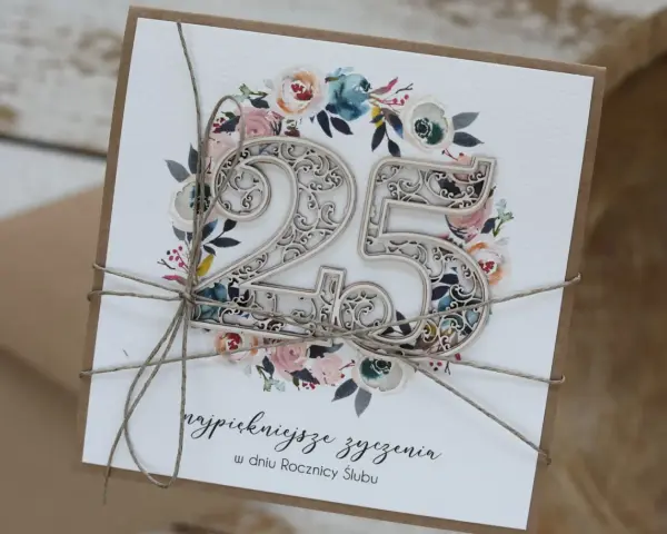 Elegancka kartka z napisem "25 lat małżeństwa jakie to gody", ozdobiona kwiatami i ażurową liczbą 25.