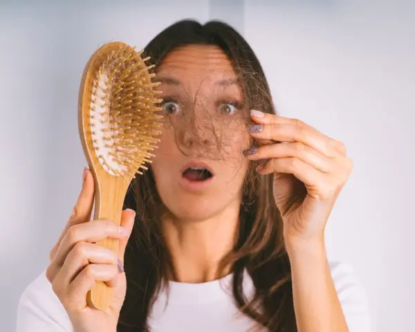 Frau mit erschrockenem Gesicht hält Haarbürste mit Haaren. Hoffnung auf progesteron haare wachsen wieder.