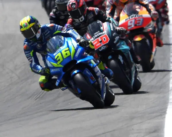 Pilotos de **MotoGP hoy** compiten en una carrera emocionante. El piloto con el número 36 en su Suzuki lidera, inclinado en una curva cerrada.