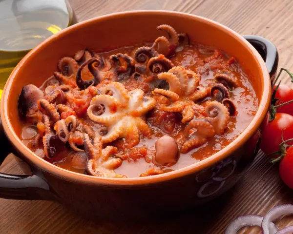 Polipetti in purgatorio, un piatto succulento con tentacoli che danzano in un sugo rosso, accompagnati da pomodorini freschi e cipolla.