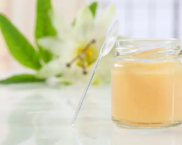 Un vasetto di pappa reale, con un fiore sullo sfondo. Alcuni credono che la pappa reale fa ingrassare, ma è un alimento nutriente.