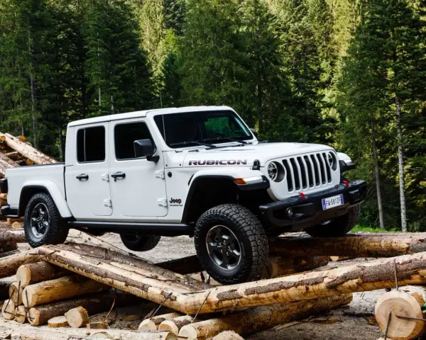 Biały jeep pickup Rubicon pokonuje przeszkodę z bali drewna w lesie.