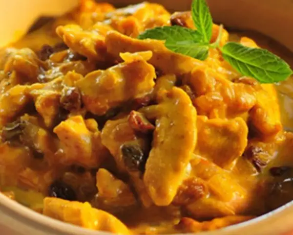 Pyszny kurczak w sosie curry z rodzynkami, ozdobiony listkiem mięty. Idealny przykład, jak zrobić sos curry do kurczaka.
