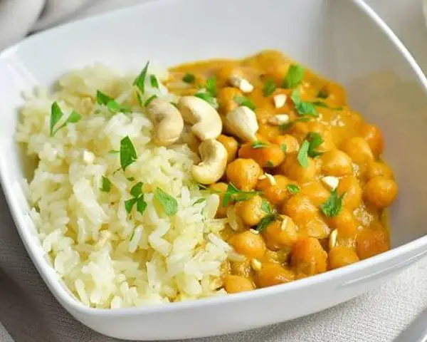 Curry de garbanzos cremoso con arroz blanco y anacardos en un cuenco blanco.