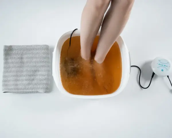 A person's feet are soaking in a foot spa with a brown solution, suggesting a method for how to remove toxins from feet naturally. A towel is nearby.