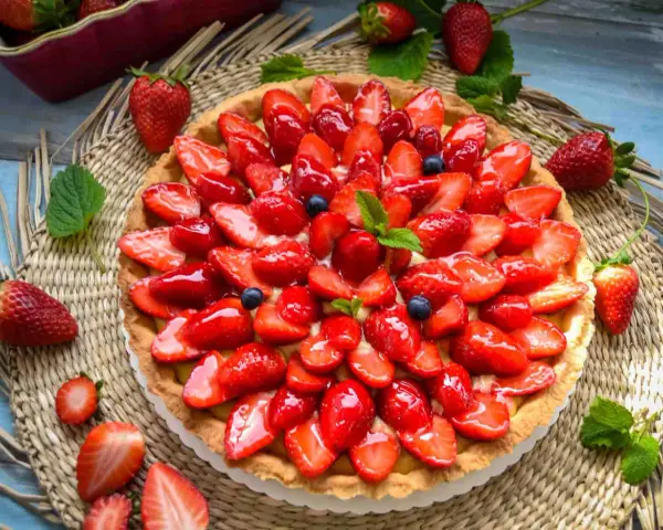 Ein leckerer Erdbeerkuchen mit einem wunderschönen Muster aus frischen Erdbeeren und Blaubeeren, glasiert und garniert mit Minze.