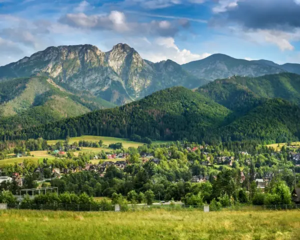 Malowniczy widok na Tatry z Jaszczurówki, gdzie liczne atrakcje czekają na turystów. Zielone wzgórza i tradycyjna zabudowa tworzą sielski krajobraz.