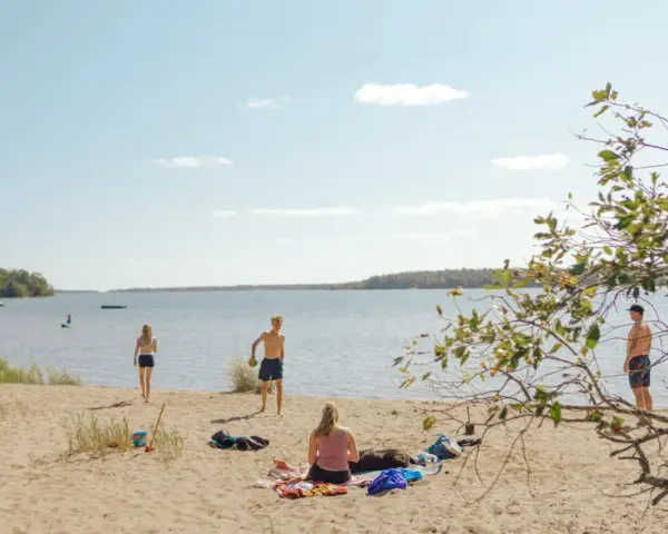 Solig dag vid Hallmare havsbad. Människor njuter på stranden, badar och leker i vattnet.