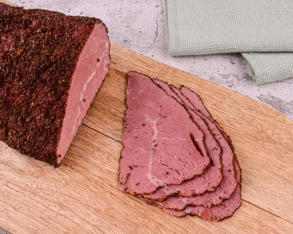 Pastrami co to? Aromatyczny, peklowany i wędzony kawałek wołowiny, pokrojony w cienkie plastry, leżący na desce.