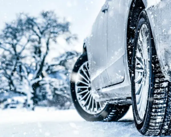 Auto im Schnee mit Winterreifen, verschneiter Baum im Hintergrund.