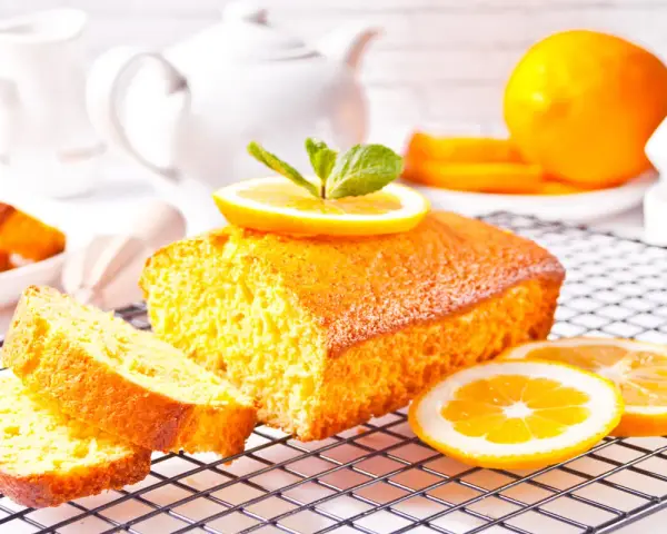 Un soffice plumcake al limone, guarnito con una fetta d'arancia e menta, su una griglia, pronto per essere gustato.