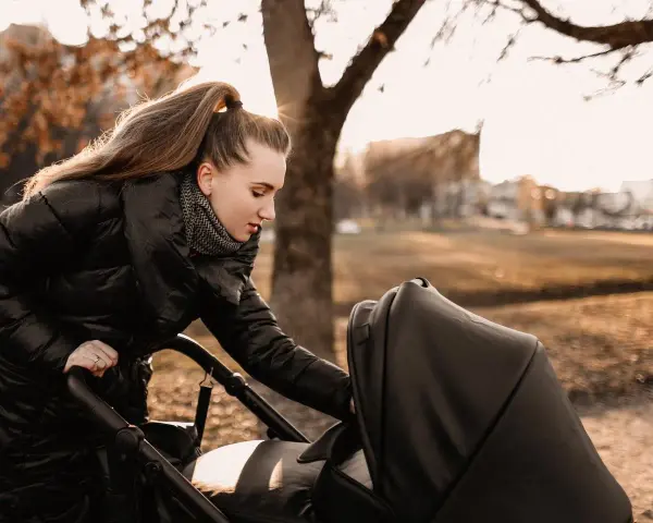 Mama przygotowuje malucha na spacer w 15 stopniach. Ciepła kurtka i szalik to podstawa, by zapewnić komfort dziecku w wózku.