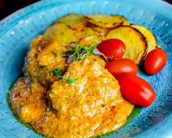 Köttbullar i krämig cafe de paris sås med rostade potatisskivor och körsbärstomater på en blå tallrik.