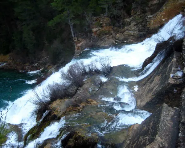 El salto de Poveda, una cascada de agua blanca y espumosa que desciende por rocas y vegetación, desemboca en un río de aguas turquesas.