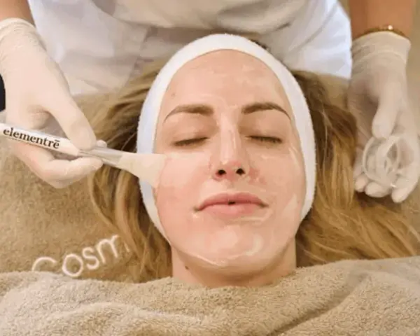 Kosmetikerin trägt eine Maske auf, um die Haut zu reinigen.