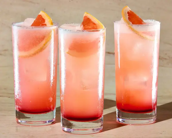 Trzy orzeźwiające drinki: Tequila Sunrise i Paloma, z plasterkami grejpfruta i lodem.
