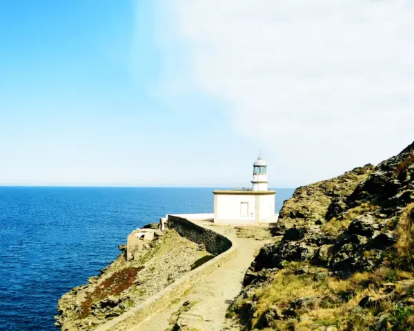 El faro de Cala Nans se alza sobre un acantilado rocoso, vigilando el azul intenso del mar Mediterráneo bajo un cielo despejado.