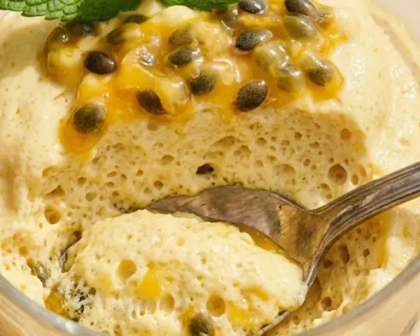 Delicioso mousse de maracuyá en vaso, coronado con pulpa y semillas de la fruta, y una hoja de menta. Una cucharada lista para disfrutar.