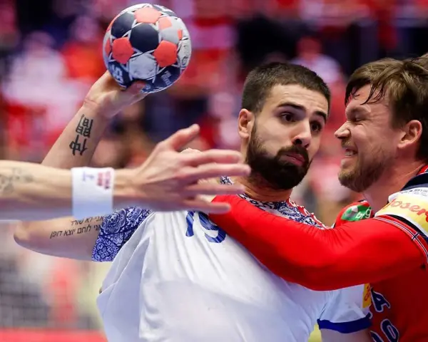 Zacięta walka na parkiecie! Piłkarz z piłką w ręku, być może z Francji, mierzy się z obrońcą z Norwegii. Emocje w piłce ręcznej sięgają zenitu.