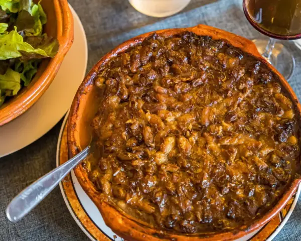 Cassoulet de Castelnaudary burbujeante en cazuela de barro, acompañado de ensalada verde y vino tinto.