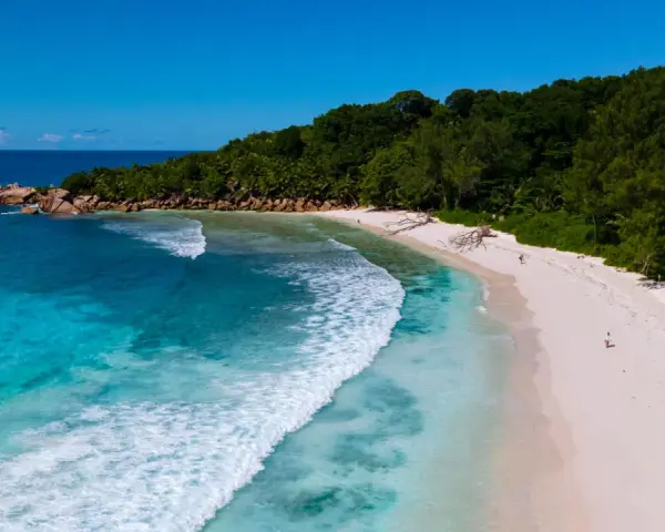 Rajska wyspa na Oceanie Indyjskim. Turkusowa woda obmywa piaszczystą plażę, a bujna zieleń porasta wzgórza.