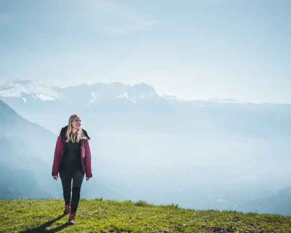 Frau in Wanderkleidung genießt die Aussicht auf verschneite Berge. Perfekt, was zieht man zum wandern an!