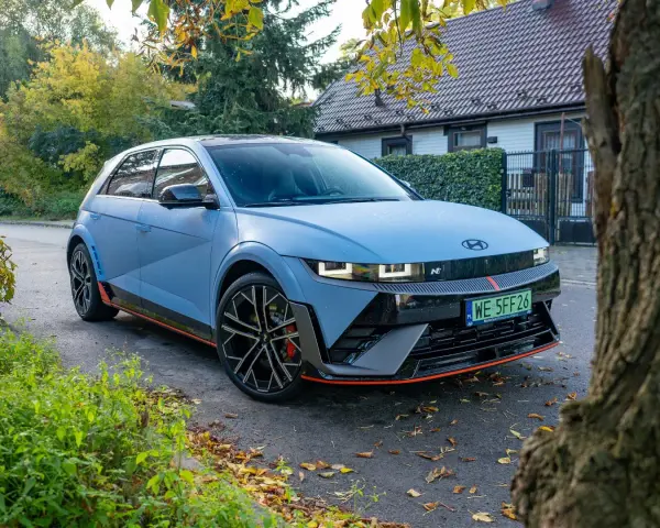 Niebieski Hyundai Ioniq 5 N z czerwonymi akcentami stoi na tle domu i drzew.