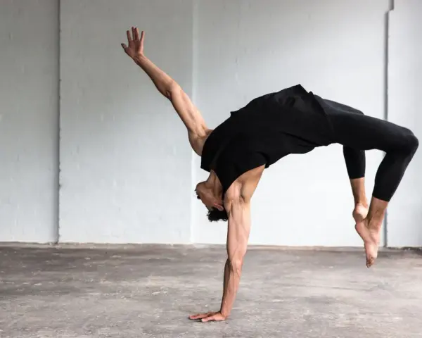 Un bailarín en un estudio blanco realiza un movimiento acrobático, mostrando que es la danza.